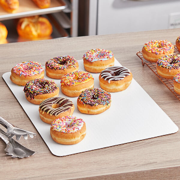 A tray of doughnuts with chocolate and white frosting and sprinkles on a Baker's Lane white half sheet cake pad.