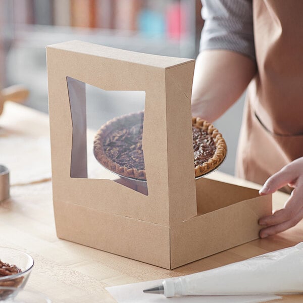 A person putting a pie into a Baker's Mark Kraft bakery box with a window.