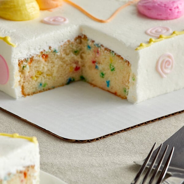 A white frosted cake with pink frosting and colorful sprinkles on a Baker's Mark full sheet cake pad.