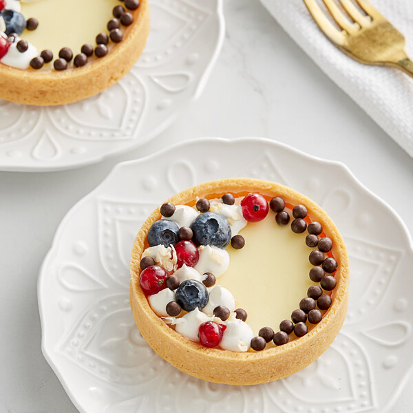 A dessert plate with two tarts topped with berries and Valrhona dark chocolate pearls.