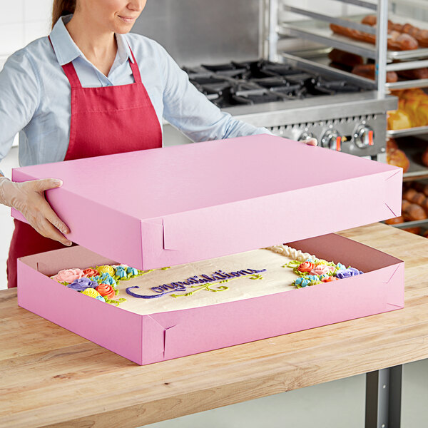 A woman holding a pink Baker's Lane bakery box with a cake inside.