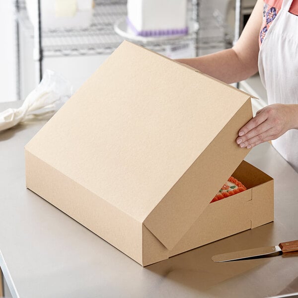 A woman opening a Baker's Mark kraft bakery box with a cake inside.