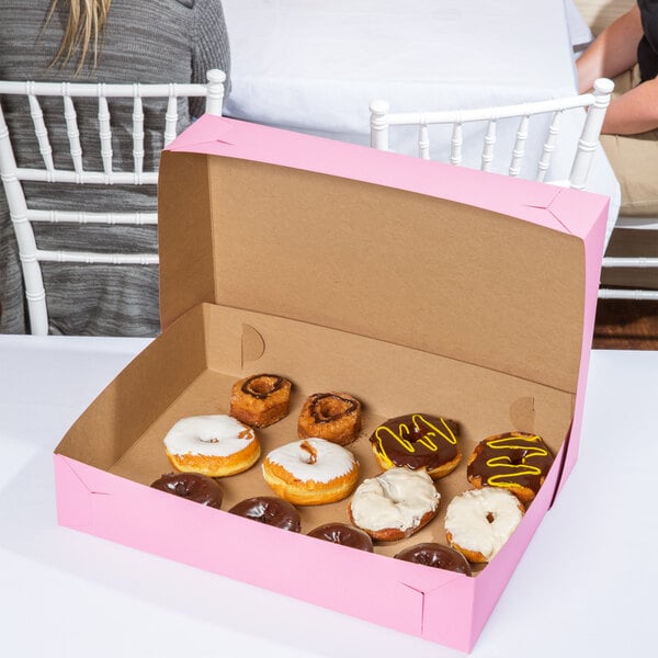 A Baker's Mark pink bakery box filled with donuts on a table at a catering event.