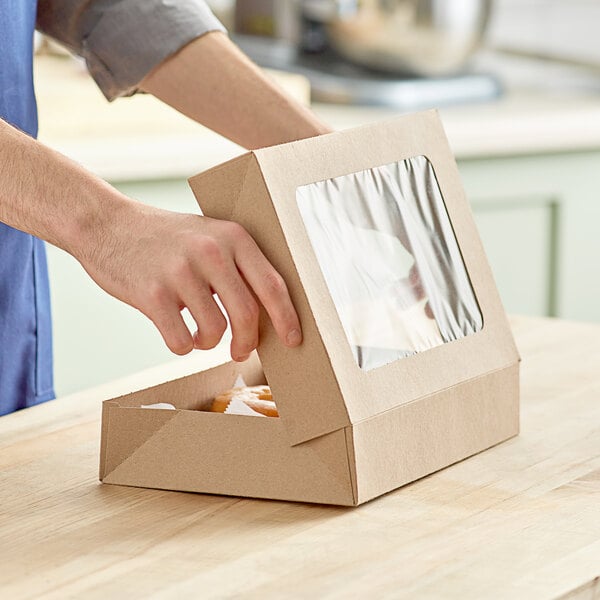 A person opening a Baker's Mark Kraft bakery box to take out a donut.