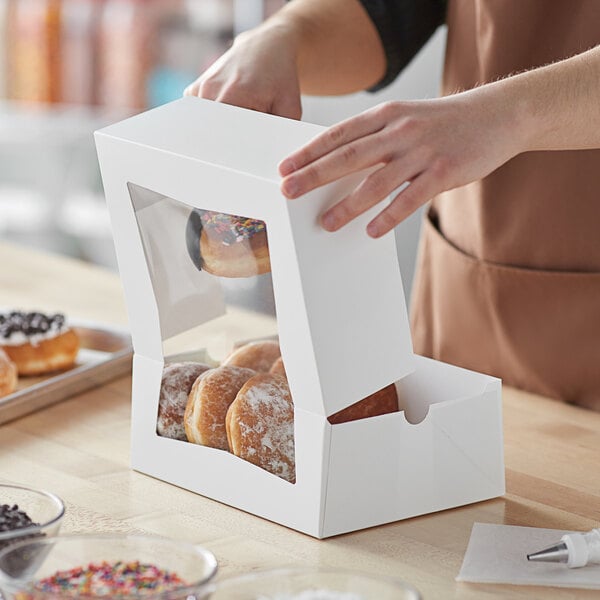 A person opening a box of doughnuts to reveal a close up of a doughnut inside.