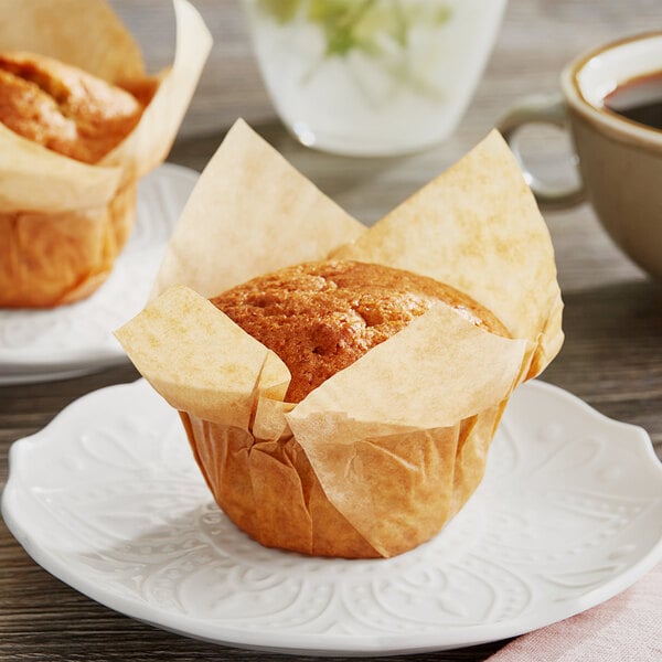 Two Baker's Mark unbleached natural Kraft muffins in paper wrappers on a plate.