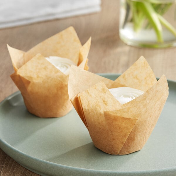 Two Baker's Mark unbleached natural kraft tulip baking cups with cupcakes inside on a white plate.