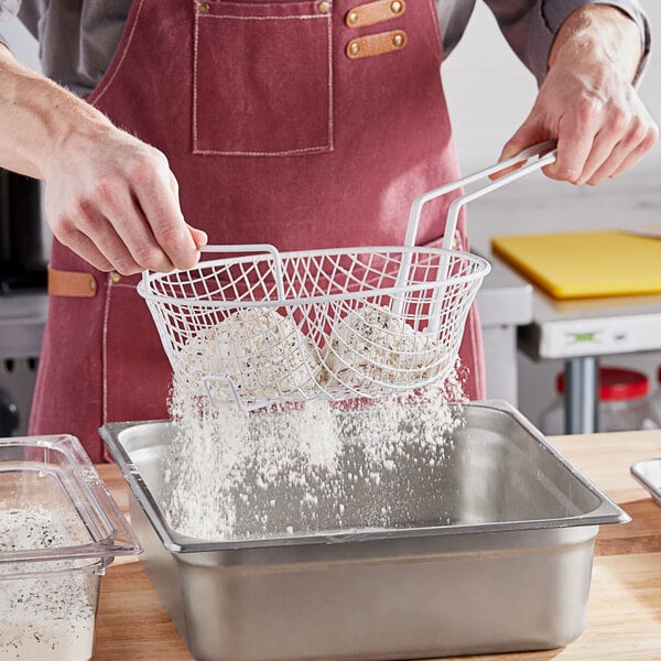 A person pouring flour into a white mesh breading basket with a helper handle.