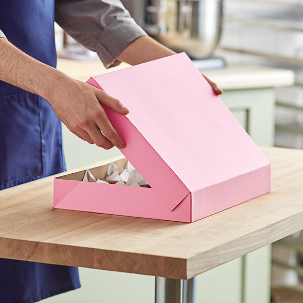 A person opening a pink Baker's Mark donut box.