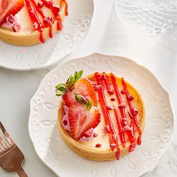 A white plate of Valrhona strawberry dessert with strawberries and red sauce.