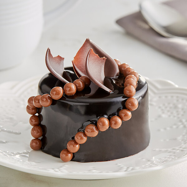 A chocolate cake with Valrhona Caramelia chocolate beads on top sitting on a plate.