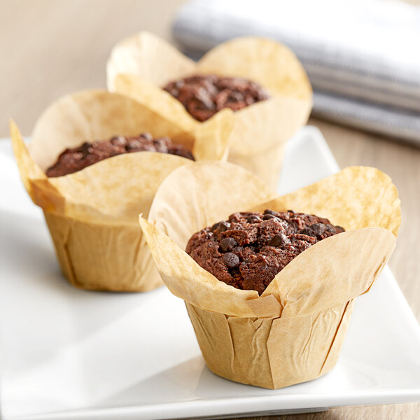 Three Baker's Mark unbleached natural kraft large rounded muffins in paper wrappers on a white plate.