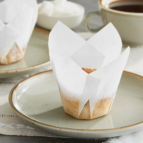 A Baker's Mark white tulip baking cup with a cupcake on a plate.