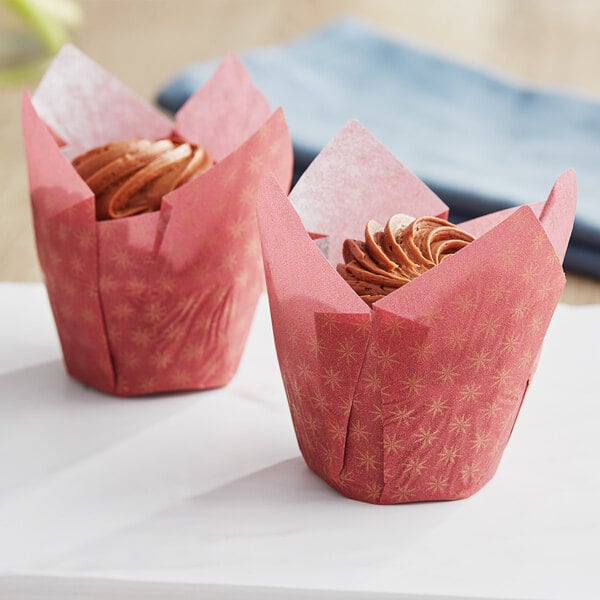 Two cupcakes in red and gold tulip baking cup wrappers with frosting.