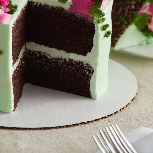 A Baker's Mark white corrugated cake circle under a chocolate cake with green frosting and flowers.