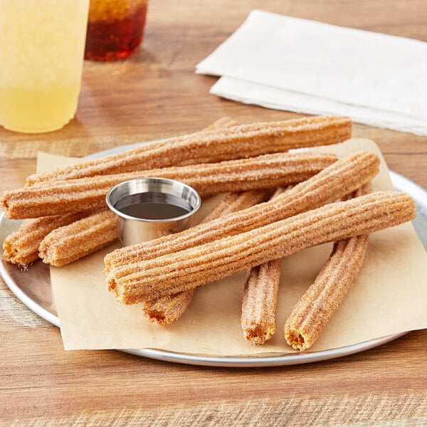 A plate of J & J Snack Foods Hola Churros cinnamon sugar churros with a cup of yellow liquid.