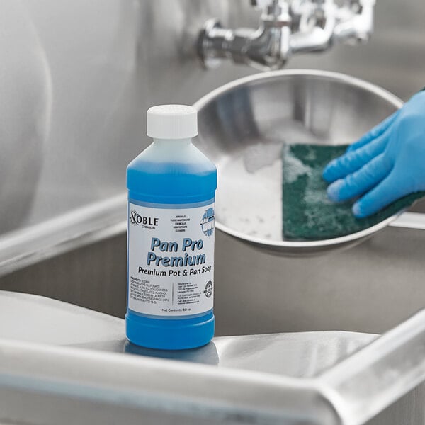 A gloved hand using Noble Chemical PRM Pan Pro to clean a sink.