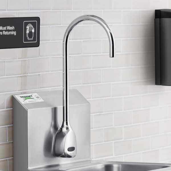 A Delta touchless wall-mount faucet with a gooseneck spout over a stainless steel sink.