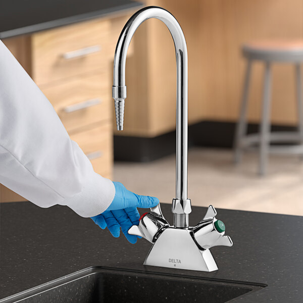 A person wearing gloves holding a Delta laboratory faucet.