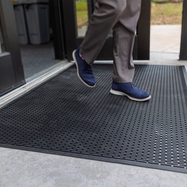 A person is stepping onto a large black rubber mat with a textured surface placed at an entrance.