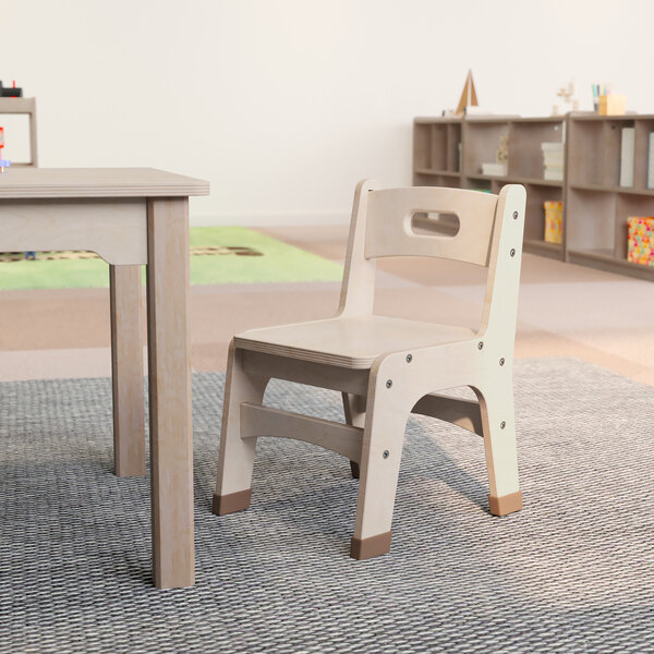 A Flash Furniture wooden classroom chair with a 10" seat height next to a wooden table.
