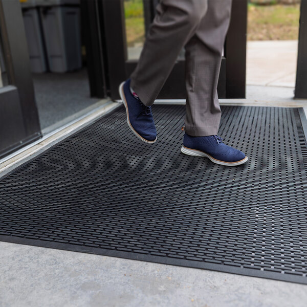 A person is stepping onto a large black rubber mat with a textured surface placed at an entrance.