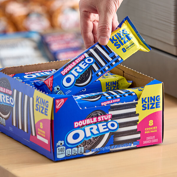 A hand holding a box of Nabisco Oreo King Size Double Stuf cookie snack packs.