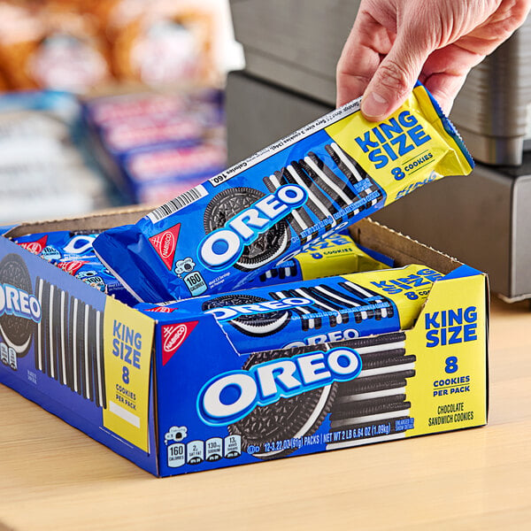 A person holding a box of Nabisco Oreo King Size cookie snack packs.