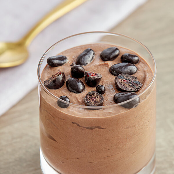 A glass of chocolate pudding with Albanese Dark Chocolate Covered Dried Cranberries and a spoon.