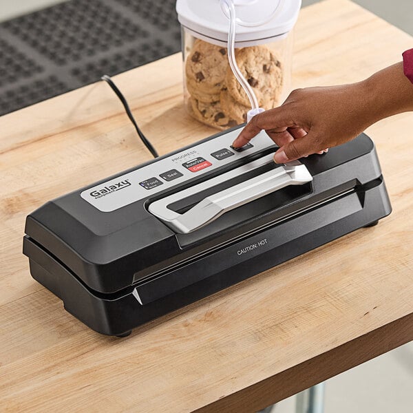 A person's hand pressing a button on a black and silver Galaxy vacuum sealer.