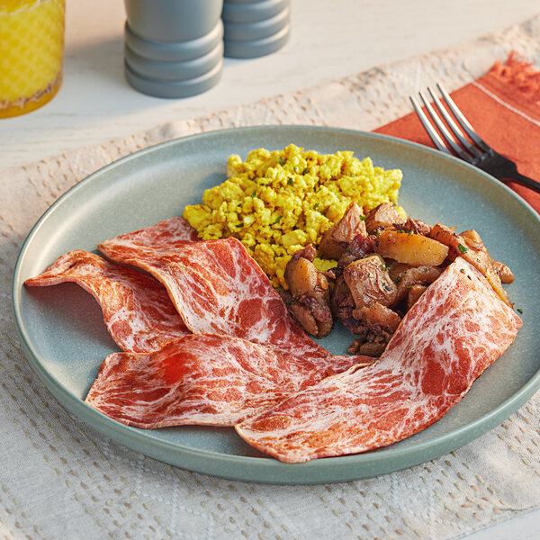 A plate of Beleaf plant-based bacon on a table with meat and potatoes.