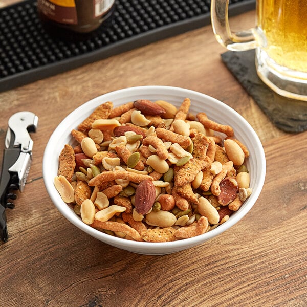 A bowl of Albanese Party Snack Mix nuts next to a glass of beer on a table.