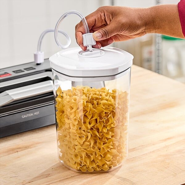 A hand using a Galaxy VC2000 vacuum canister to store noodles.
