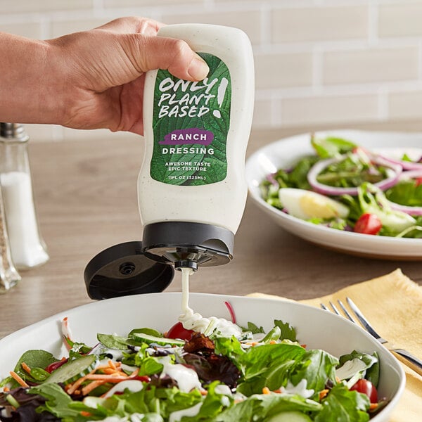 A hand pouring Only Plant Based! Vegan Ranch Dressing into a bowl of salad.