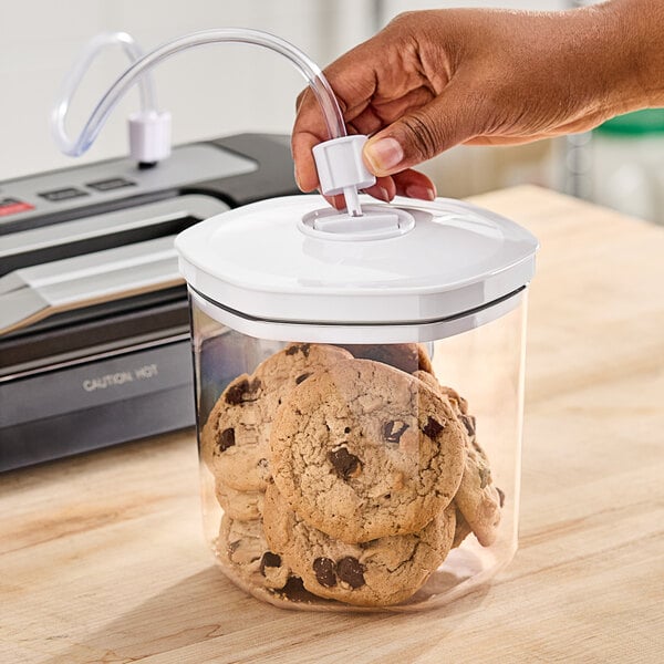 A hand opening a Galaxy vacuum canister of cookies on a kitchen counter.
