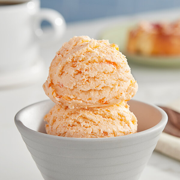 A white bowl of I. Rice orange pineapple hard serve ice cream with a scoop of ice cream on top.