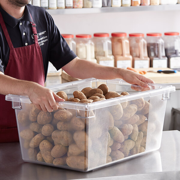 A person in a red apron using a VacPak-It clear water bin to hold potatoes.