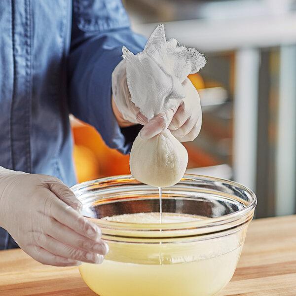 A person holding a white Fox Run cheesecloth bag over a bowl of liquid.