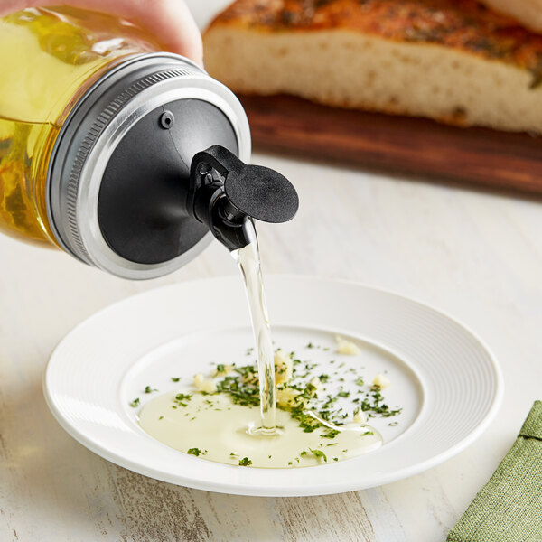 A person pouring yellow liquid from a Fox Run Oil & Vinegar Cruet Lid into a bowl.