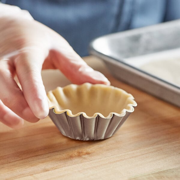 A person holding a Fox Run round fluted tart tin with a pie crust inside.