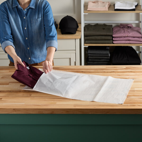 A woman holding a white Vela paper bag with a folded shirt inside.