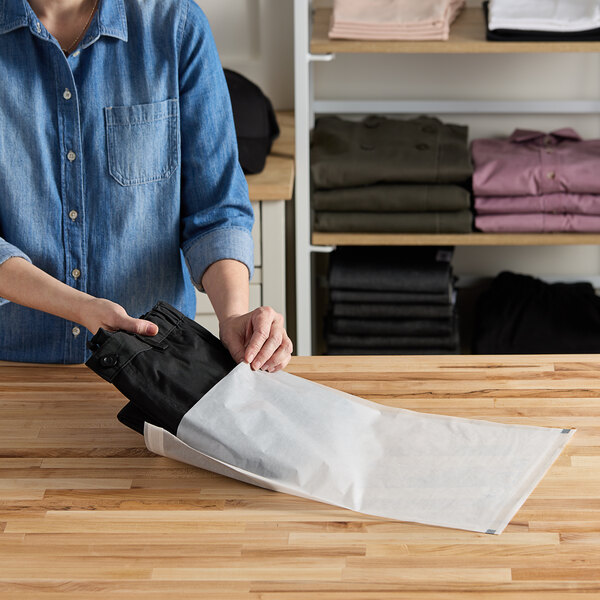 A person putting black clothes into a white Vela layflat shipping bag.