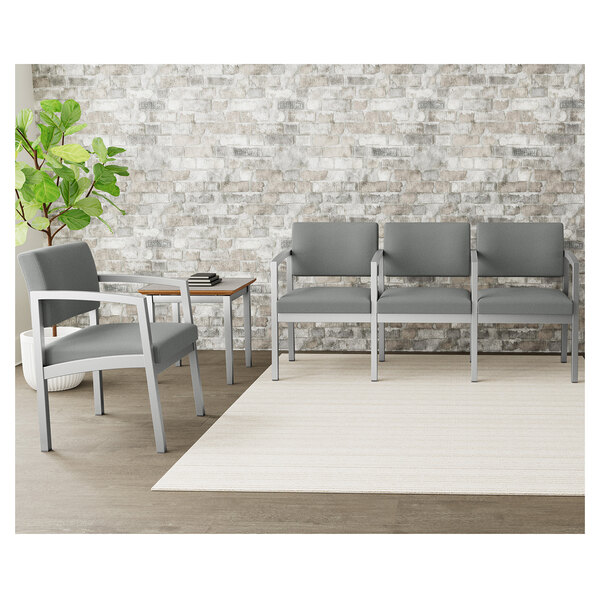 A Lesro Lenox steel sofa with asteroid fabric and center arms in a lounge area with a table and chairs in front of a brick wall.