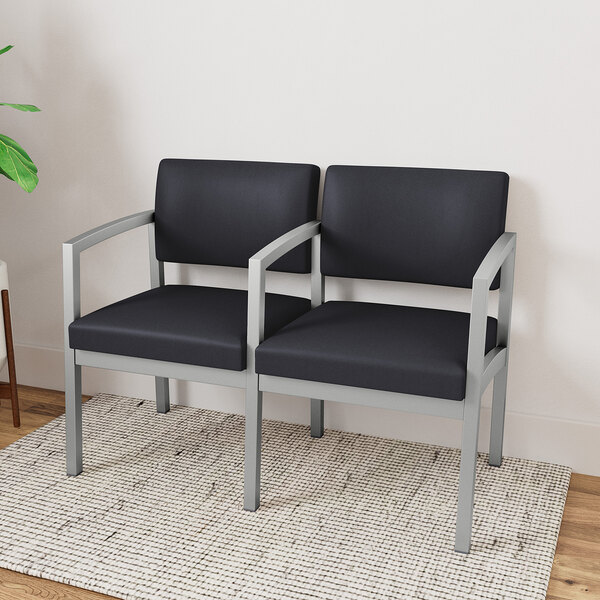 A Lesro Lenox black vinyl loveseat with a center arm on a rug.