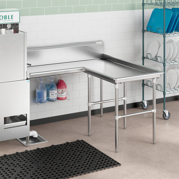 A stainless steel L-shape dishtable with a sink on the right and detergent bottles on the shelf.