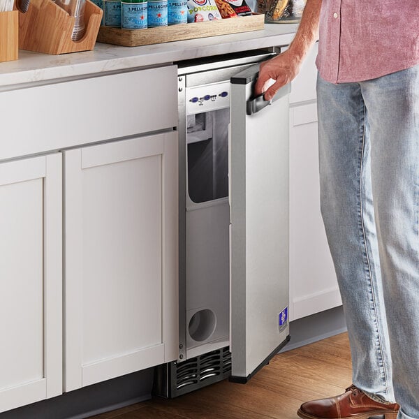 A man standing in front of a Manitowoc undercounter ice machine with the door open.