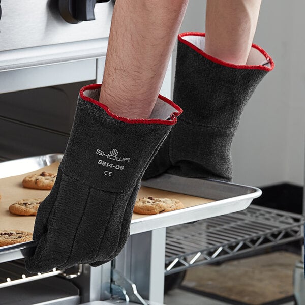 A person wearing Showa black neoprene heat-resistant gloves takes a tray of cookies out of the oven.