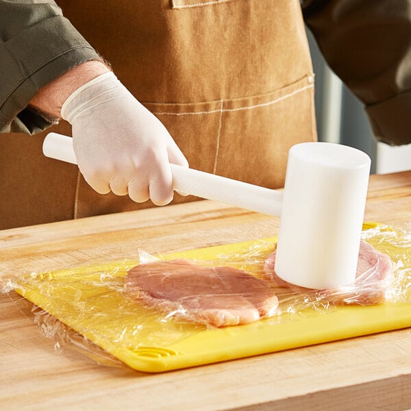 A person using a Choice plastic meat mallet to tenderize a piece of meat.