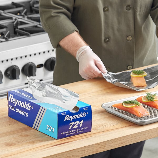 A person wearing gloves using Reynolds pop-up aluminum foil sheets to wrap a piece of salmon.