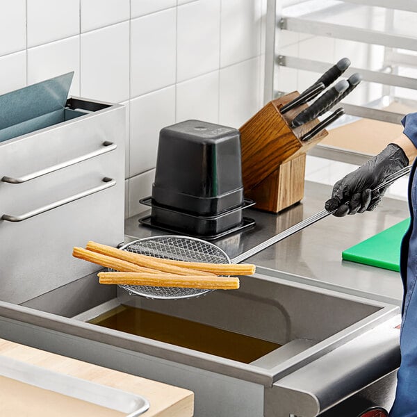 A woman using a Choice 8" round coarse mesh skimmer to fry food in a fryer.